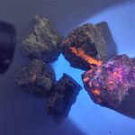 Glühender Feuerstein unter UV-Licht, zeigt leuchtende orange und pinkfarbene Flecken auf dunklem Gestein, ideal für wissenschaftliche Dekorationen und Experimente.