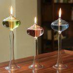 Drei elegante Glasgefäße mit brennenden Flüssigkeiten in verschiedenen Farben auf einem Holztablett.