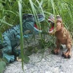 Zwei Dinosaurier-Spielzeuge, ein grüner und ein brauner, in einem natürlichen Umfeld mit Gras und Steinen, ideal für Kinder und Sammler.
