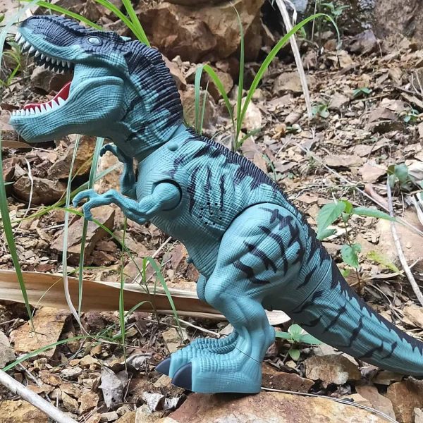 Realistisches Dinosaurier-Spielzeugmodell im Freien, detailreich gestaltet mit blauer Haut und schwarzen Streifen, auf einem Boden aus Erde und Steinen.