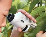 Kind mit tragbarem Mikroskop, das Blätter und Pflanzen in der Natur untersucht, ideal für Wissenschafts- und Naturbegeisterte.