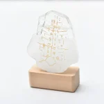 Dekorativer Stein mit goldenen ägyptischen Hieroglyphen auf transparentem Glas, auf Holzsockel präsentiert.