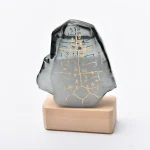 Dekorativer Stein mit goldenen Hieroglyphen auf schwarzer Oberfläche, auf Holzsockel präsentiert, inspiriert von ägyptischer Kultur.