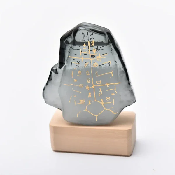 Dekorativer Stein mit goldenen Hieroglyphen auf schwarzer Oberfläche, auf Holzsockel präsentiert, inspiriert von ägyptischer Kultur.