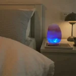 Moderne Stehlampe mit blauer LED-Beleuchtung auf Nachttisch neben Bett, gemütliche Schlafzimmerdekoration, entspannte Atmosphäre.