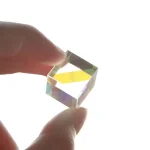 Transparentes Kristallquadrat, das Licht bricht und Regenbogenfarben zeigt, gehalten zwischen Daumen und Zeigefinger.