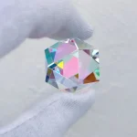 Hochwertiger, prismatischer Kristall mit Regenbogeneffekten, gehalten zwischen zwei Fingern. Perfekt für wissenschaftliche Dekorationen und Sammlerstücke.