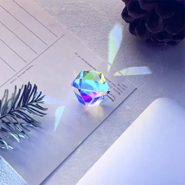 Glitzernder, sternförmiger Kristall, der Licht bricht und schillernde Farben auf einer weißen Oberfläche reflektiert, umgeben von Dekorationsgegenständen und Papier.