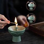 Ein grünes Kerzenfeuerzeug, das eine Kerze anzündet, mit einer Hand, die ein Zündholz hält, auf einem dunklen Tisch.
