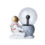 Niedliche Raumfahrer-Figur neben einer Mond- und Glaskugel-Dekoration, ideal für wissenschaftliche und dekorative Zwecke.