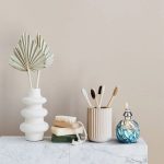 Stilvolle Badezimmerdekoration mit weißen Zahnbürsten in einer eleganten Vase, einem Duftölfläschchen und natürlichen Accessoires auf einem weißen Marmortisch.