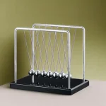 Das Newtonsches Pendel mit sechs metallischen Kugeln auf schwarzem Sockel, ideal für physikalische Demonstrationen und wissenschaftliche Dekorationen.