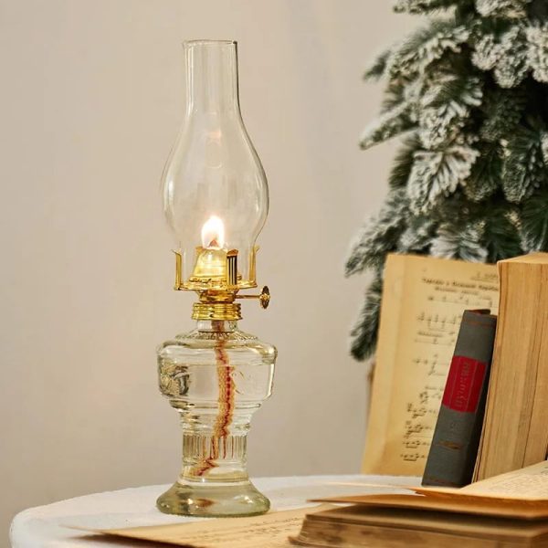 Antike Kerzenlampe aus Glas mit brennender Kerze, dekorativ auf einem weißen Tisch neben Büchern und einem Weihnachtsbaum. Perfekt für wissenschaftliche Dekorationen und nostalgisches Ambiente.