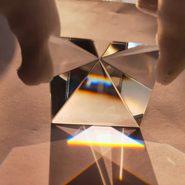 Nahaufnahme eines Kristallprismas, das Licht bricht und bunte Reflexionen auf einer glatten Oberfläche erzeugt. Perfekt für wissenschaftliche Dekorationen und Experimente.