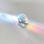Ein kleiner, schimmernder Kristallball, der Licht bricht und Regenbogenfarben auf einer weiĂen OberflĂ€che projiziert.