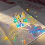 Holografischer Kristall in Blumenform, der auf einem Buch liegt, erzeugt bunte Lichtreflexionen.