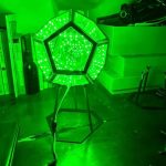 Leuchtendes geometrisches Science-Fiction-Objekt mit grünen LED-Lichtern, auf einem schwarzen Stativ in einem modernen Raum. Perfekt für Science-Fiction-Dekorationen und wissenschaftliche Themen.
