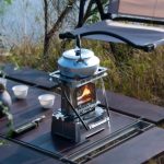Tragbarer Campingkocher mit Wasserkocher auf einem Outdoor-Tisch, ideal für Camping und Outdoor-Aktivitäten.