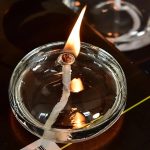 Brennende Kerze in einer transparenten Glasschale, die Flamme leuchtet hell und erzeugt eine warme Atmosphäre.