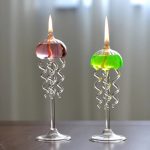 Zwei stilisierte Kerzen mit spiralförmigen Glaskörpern, die auf eleganten Glasständern stehen, eine mit rosa und die andere mit grüner Flamme, ideal für wissenschaftliche Dekorationen.