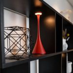 Elegante rote Tischlampe mit modernem Design, ideal für wissenschaftliche Dekorationen und Gadgets, auf einer schwarzen Regalfläche präsentiert.