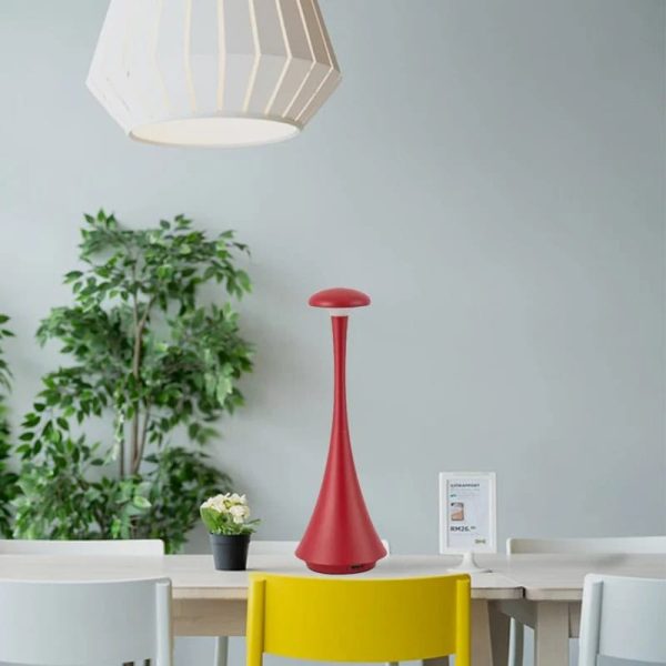 Elegante, rote Tischlampe mit schlankem Design auf einem weißen Tisch, umgeben von Pflanzen und moderner Dekoration, ideal für stilvolle Wohn- oder Büroräume.