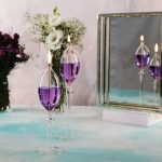 Elegante schwebende Kerzen in transparenten Glasvasen mit violettem Wachs, dekorativ auf einem Tisch mit Blumen und Spiegel.
