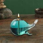 Elegantes, handgefertigtes Glas-Teelicht in Form eines Wals, ideal für wissenschaftliche Dekorationen und Geschenke, mit brennender Flamme auf einem Holztisch.