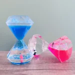 Dekorative Sanduhr mit blauen, pinken und transparenten Wasserfüllungen, verziert mit kleinen Pinguinen, ideal für wissenschaftliche Dekorationen und moderne Raumgestaltung.