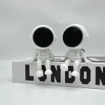 Zwei weiße Roboter im Weltraum-Design sitzen auf einem weißen Block mit "LONDON" Schriftzug, ideal für Science-Fiction- und Raumfahrt-Dekorationen.