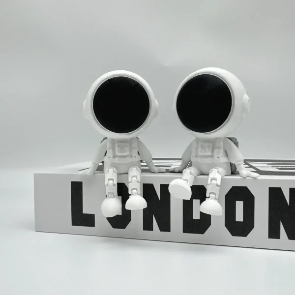 Zwei weiße Roboter im Weltraum-Design sitzen auf einem weißen Block mit "LONDON" Schriftzug, ideal für Science-Fiction- und Raumfahrt-Dekorationen.
