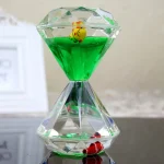 Dekoratives Glaskunststück mit Wasseruhr, grüner Flüssigkeit und kleinen Figuren, ideal für wissenschaftliche oder dekorative Zwecke.