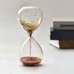 Dekorative Sanduhr mit goldenen Partikeln und rotem Sand, ideal als wissenschaftliches Dekorationsstück oder Geschenk.