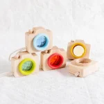Kleine Holz-Kameras mit farbigen Objektivringen in Blau, Rot, Gelb und Grün, ideal für Spielzeug oder Dekoration im wissenschaftlichen Stil.