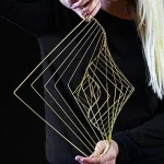 Goldfarbener Drahtschmuck in geometrischem Design, gehalten von einer Person, ideal als wissenschaftliche Dekoration oder modisches Accessoire.