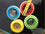 Vier bunte Kugeln mit transparenten, facettierten Innenkugeln, die auf einer schwarzen Oberfläche liegen, mit einem Maßband zur Größenbestimmung.