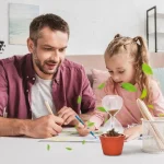 Ein Mann und ein Mädchen führen gemeinsam ein wissenschaftliches Experiment mit einer Glaskugel, Sand und Pflanzen durch, um Naturwissenschaften zu erforschen.