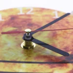 Detaillierte Nahaufnahme einer Uhr mit buntem, herbstlich inspiriertem Zifferblatt und schwarzen Zeigern, die die Zeit anzeigen.