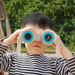 Kind mit bunten Spielzeug-Binokular, das im Freien benutzt wird, um die Natur zu erkunden. Perfekt für Kinder, die Wissenschaft und Natur entdecken möchten.