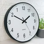 Moderne Wanduhr mit klarer Ziffernblattgestaltung, schwarzem Rahmen und präzisem Quarz-Uhrwerk, ideal für Büro oder Zuhause.