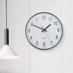 Runde Wanduhr mit weißem Zifferblatt, schwarzen Zahlen und Zeigern, ideal für moderne Innenräume und Büros.