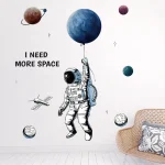 Wanddekoration mit Astronaut, der einen Planeten als Ball hält, und weiteren Planeten im Hintergrund, mit dem Text "I NEED MORE SPACE".