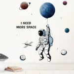 Illustration eines Astronauten, der einen Planeten als Ball hält, mit weiteren Planeten im Hintergrund und dem Text "I NEED MORE SPACE" in einer modernen Wandgestaltung.