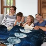 Familie sitzt auf einer Couch mit einer Decke, die den Nachthimmel mit Mond- und Sternmotiven zeigt, ideal für gemütliche Abende und Kinderzimmerdekoration.