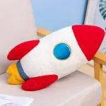 Plüschtier in Form eines Raumfahrzeugs mit rotem, weißem und gelbem Design, ideal als Dekoration oder Kuscheltier.