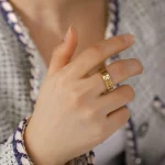 Nahaufnahme einer Hand mit einem goldenen Ring, getragen von einer Person in einem karierten Hemd, vor einem unscharfen Hintergrund.