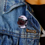 Detailaufnahme eines Ansteckpins mit Weltraummotiv, befestigt an einer Jeansjacke, zeigt ein Tier im Astronautenhelm.