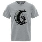Graues T-Shirt mit einem künstlerischen Druck eines Astronauten, der auf einer Mondkrater-ähnlichen Oberfläche steht, umgeben von Sternen und Galaxien.