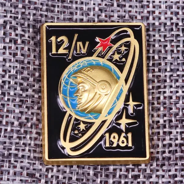 Detailaufnahme eines Raumfahrt-Abzeichens aus dem Jahr 1961 mit Astronauten-Design, goldene und blaue Akzente, auf einem Stoffhintergrund.