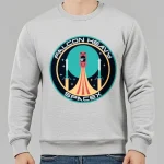 Logo des Falcon Heavy Raumfahrtprogramms von SpaceX, mit Rakete, Sternen und Planeten im Hintergrund, auf einem grauen Sweatshirt.